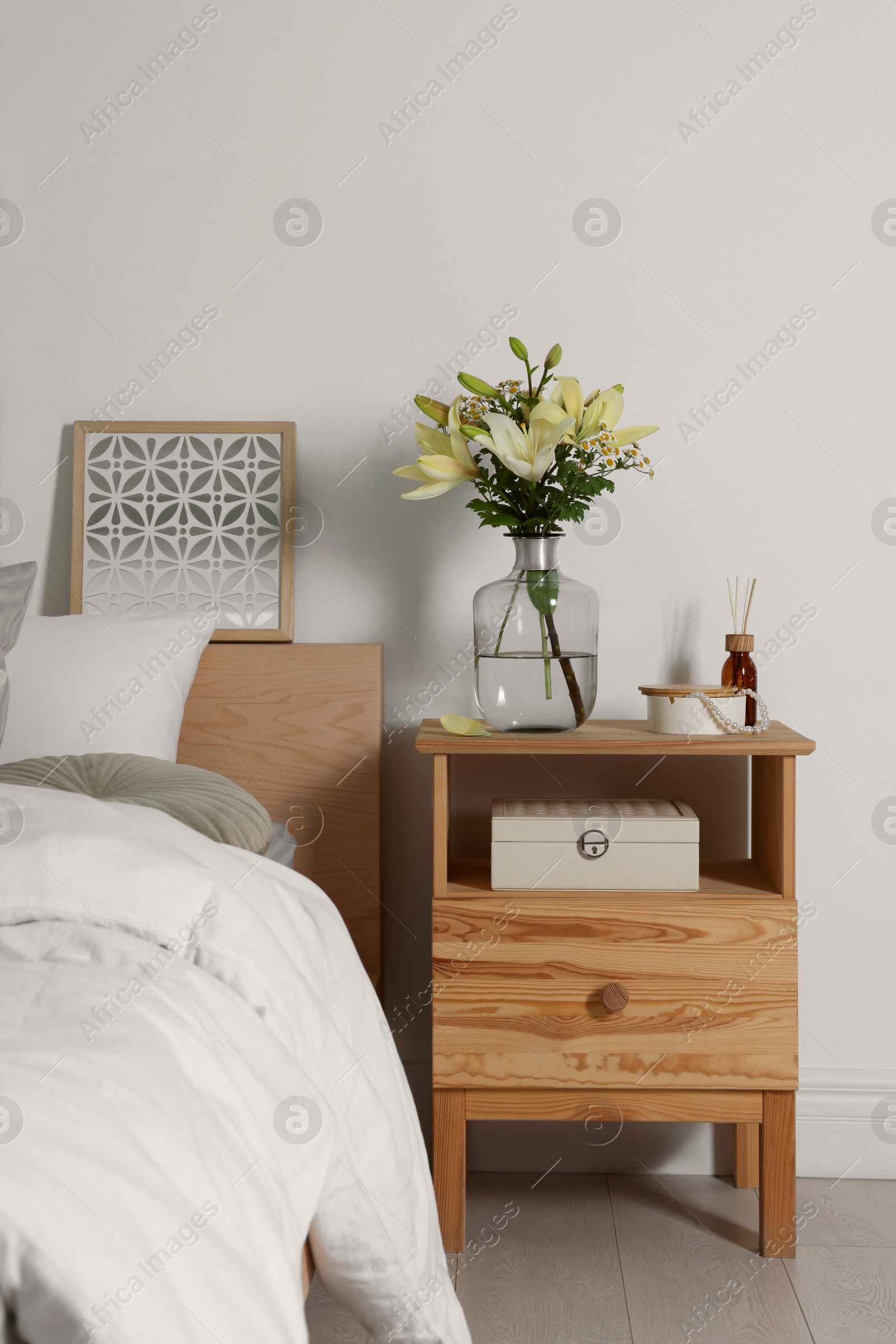 Photo of Vase with bouquet of fresh flowers on wooden nightstand in bedroom