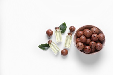 Photo of Delicious organic Macadamia nuts, green leaves and natural oil on white background, flat lay. Space for text