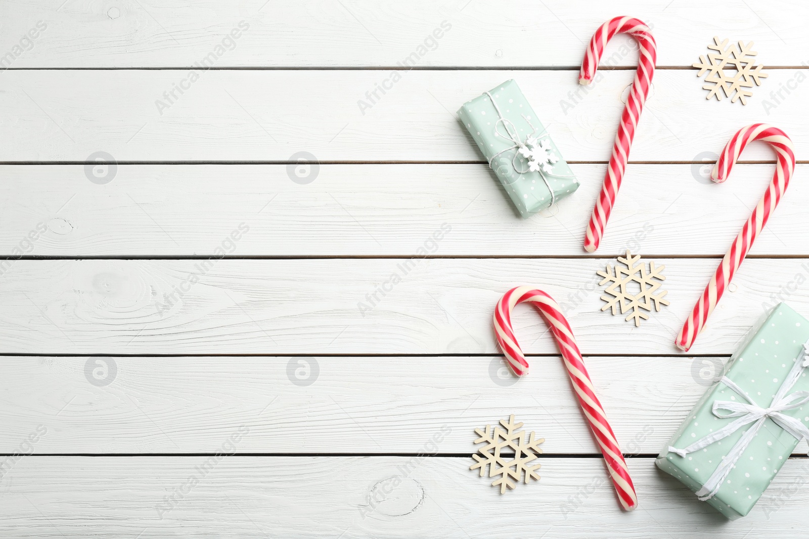 Photo of Candy canes, Christmas gifts and snowflakes on white wooden table, flat lay. Space for text