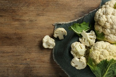 Photo of Cut and whole cauliflowers on wooden table, top view. Space for text