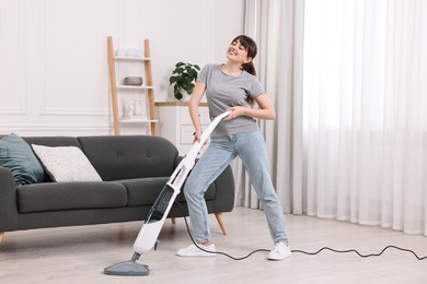 Happy young housewife cleaning floor with steam mop at home