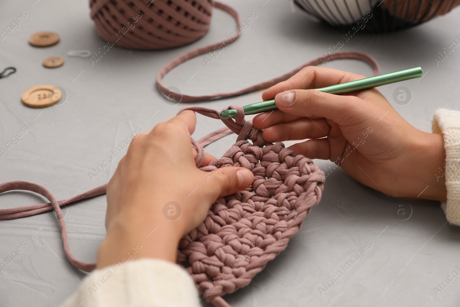 Photo of Woman crocheting with threads at grey table, closeup. Engaging hobby