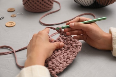Photo of Woman crocheting with threads at grey table, closeup. Engaging hobby