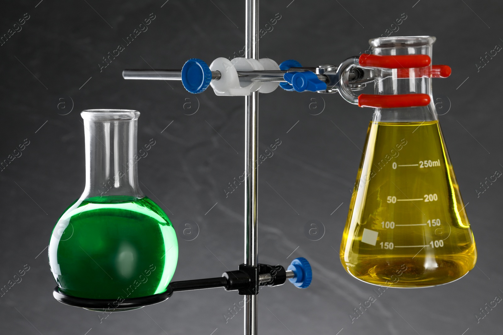 Photo of Retort stand and laboratory flasks with liquids on grey background