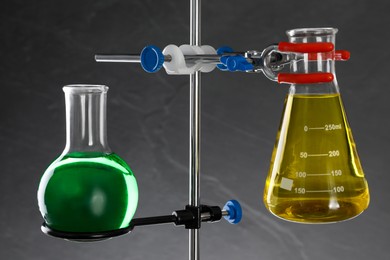 Photo of Retort stand and laboratory flasks with liquids on grey background
