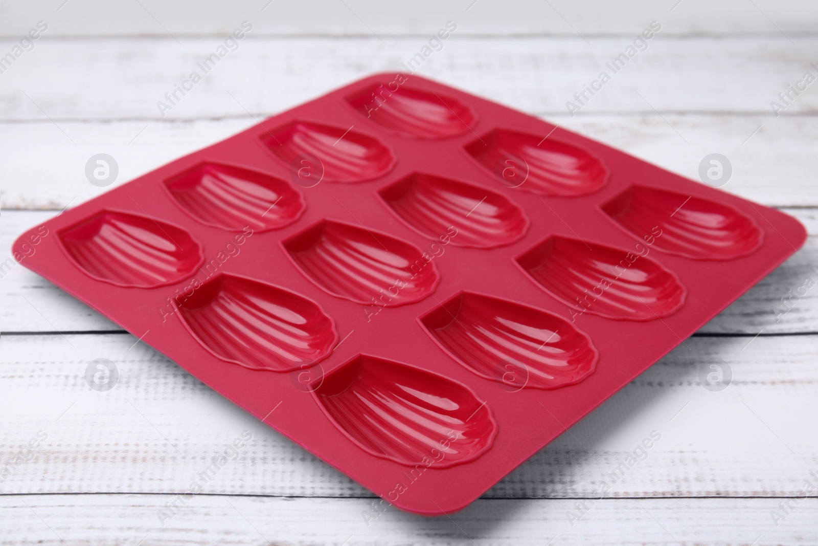 Photo of Red baking mold for madeleine cookies on white wooden table, closeup