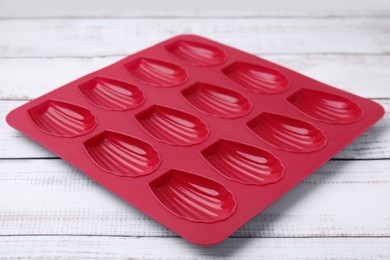 Red baking mold for madeleine cookies on white wooden table, closeup