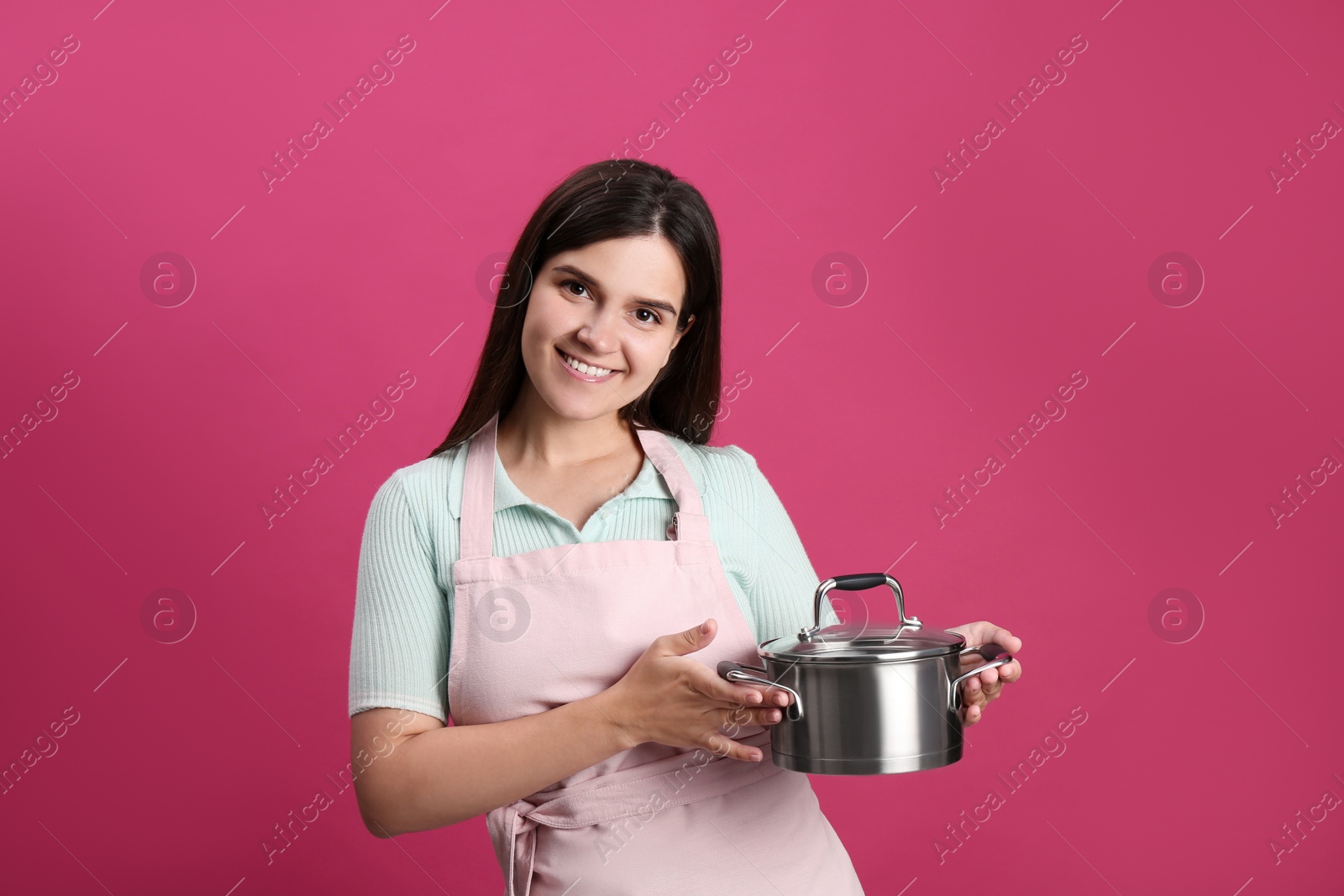 Photo of Happy young woman with cooking pot on pink background