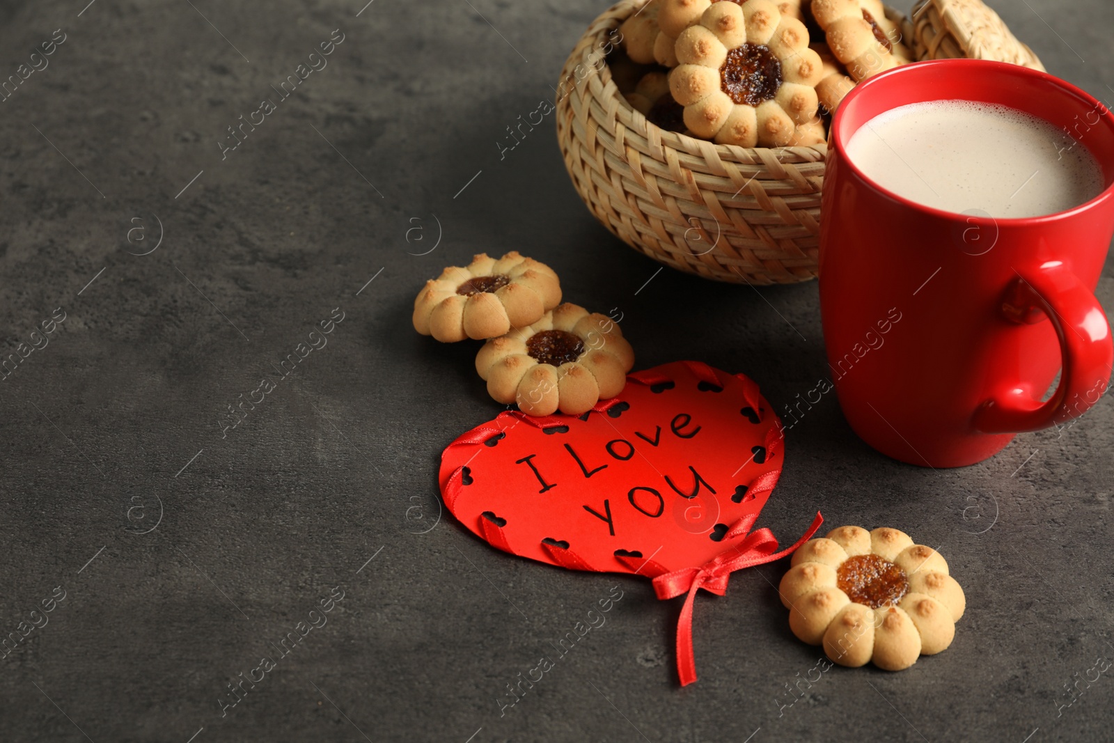 Photo of Heart shaped greeting card with phrase I Love You near cookies and red cup on dark grey table