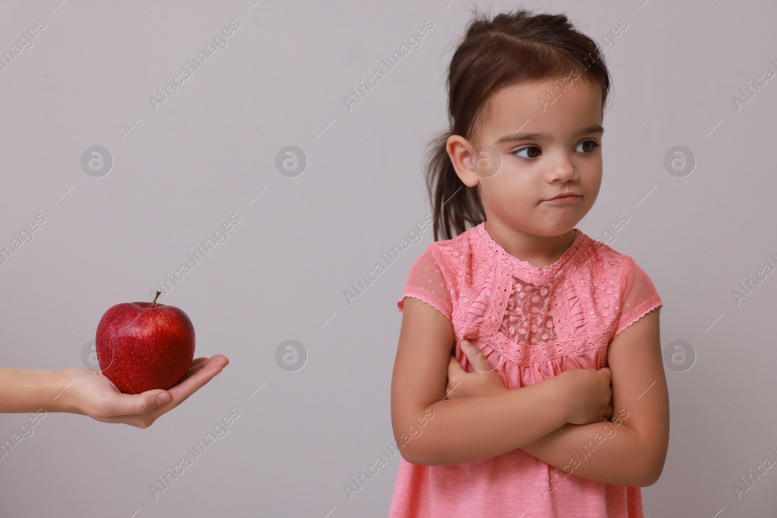 Photo of Cute little girl refusing to eat apple on grey background