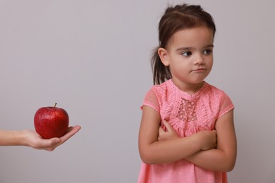 Photo of Cute little girl refusing to eat apple on grey background