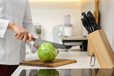 Photo of Professional chef cutting cabbage at white countertop in kitchen, closeup
