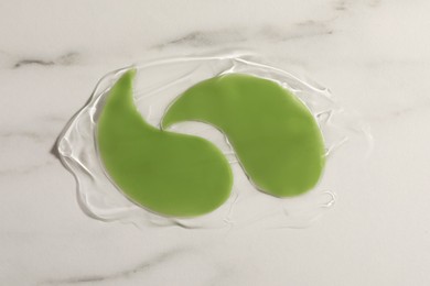 Green under eye patches with gel on white marble background, top view. Cosmetic product