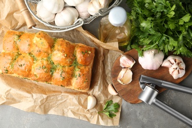 Photo of Buns of bread with garlic and herbs on grey table, flat lay