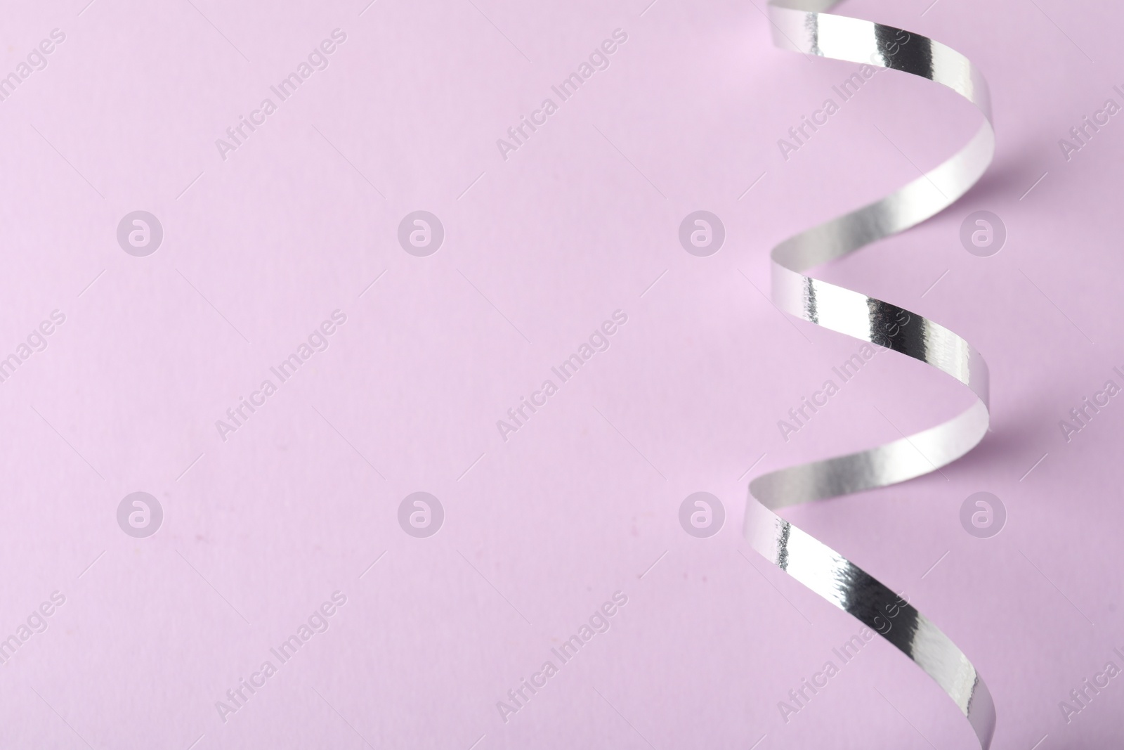 Photo of Shiny serpentine streamer on lilac background, top view. Space for text