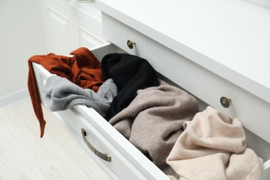 Photo of Cluttered chest of drawers indoors. Clothes in mess