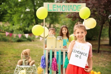 Photo of Little girl holding price tag near lemonade stand in park