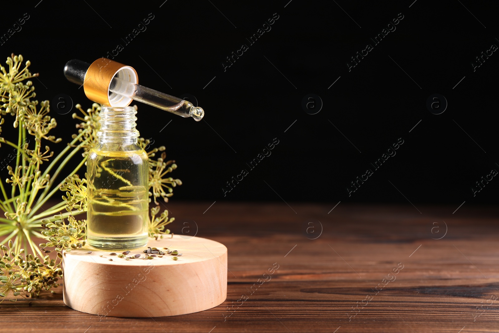 Photo of Bottle of essential oil, pipette and fresh dill on wooden table against black background. Space for text