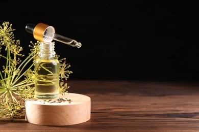 Bottle of essential oil, pipette and fresh dill on wooden table against black background. Space for text