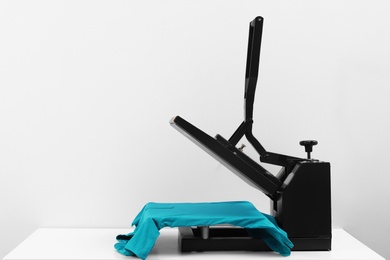 Heat press machine with t-shirt on table against light background, space for text