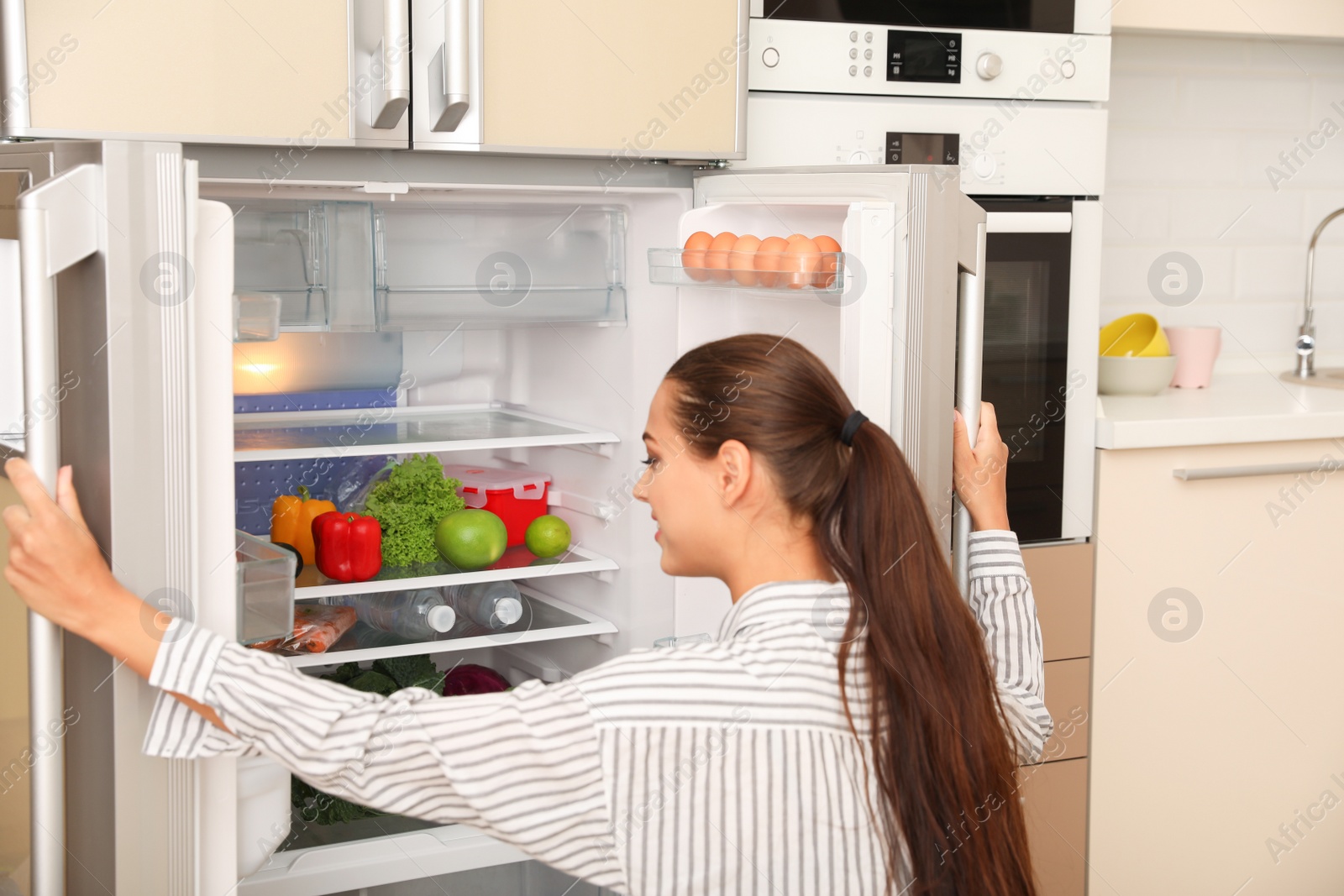 Photo of Young woman choosing products from refrigerator in kitchen