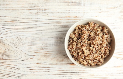 Photo of Cooked delicious quinoa in bowl on wooden table, top view. Space for text