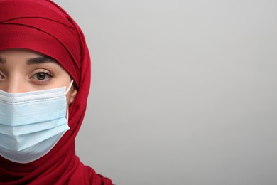 Photo of Muslim woman in hijab and medical mask on light gray background, closeup. Space for text