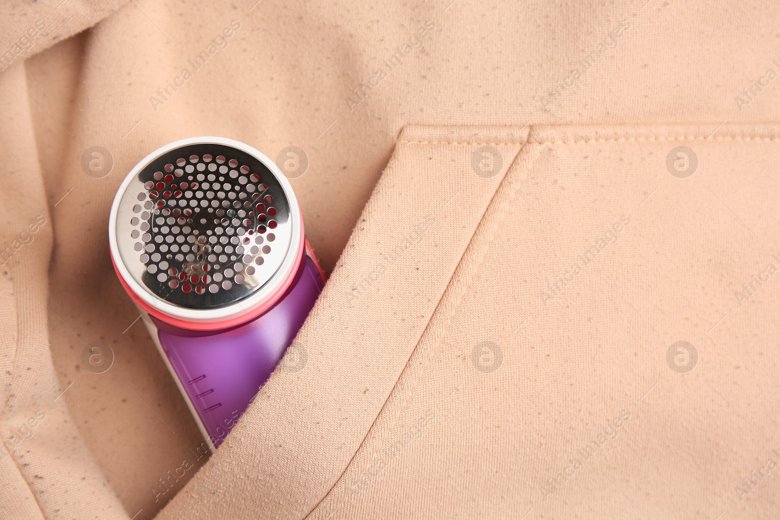 Photo of Fabric shaver in pocket of beige sweatshirt with lint, top view