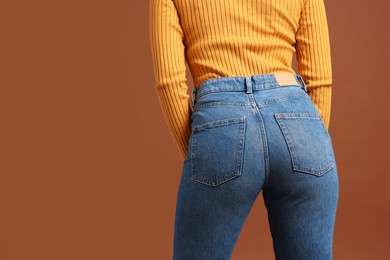 Woman in stylish jeans on brown background, closeup. Space for text