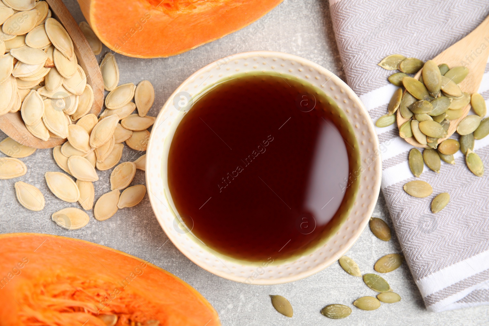 Photo of Bowl of oil and pumpkin seeds on light grey table, flat lay