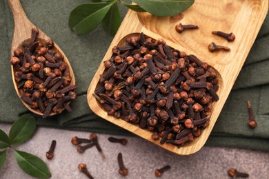 Photo of Wooden tray with aromatic cloves, spoon and green leaves on table, flat lay