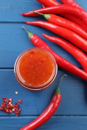 Photo of Spicy chili sauce in jar and peppers on blue wooden table, flat lay