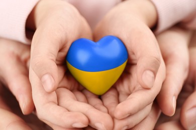 Image of Stop war in Ukraine. Family holding heart shaped toy with colors of Ukrainian flag in hands, closeup