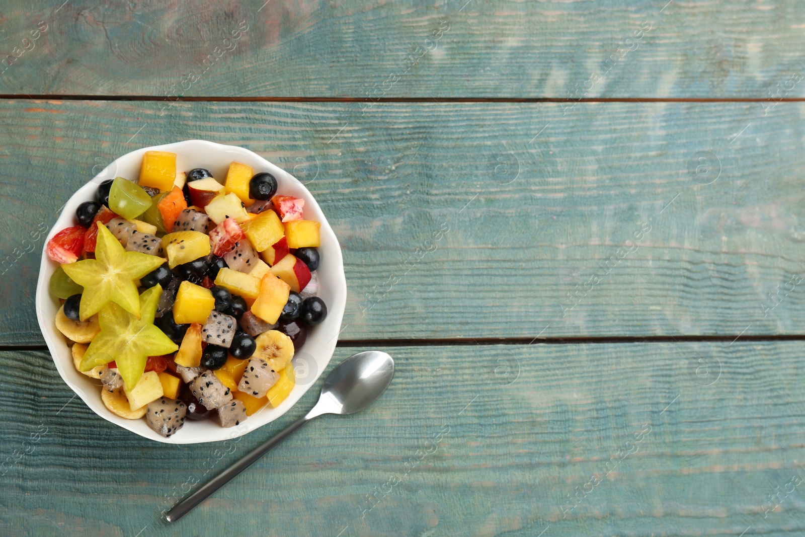 Photo of Delicious exotic fruit salad and spoon on light blue wooden table, flat lay. Space for text