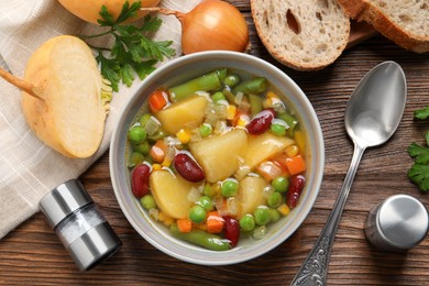 Photo of Bowl of delicious turnip soup served on wooden table, flat lay