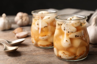 Photo of Preserved garlic in glass jars on wooden table, closeup. Space for text