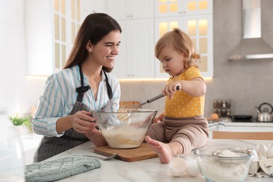 Photo of Mother and her little daughter cooking dough together in kitchen