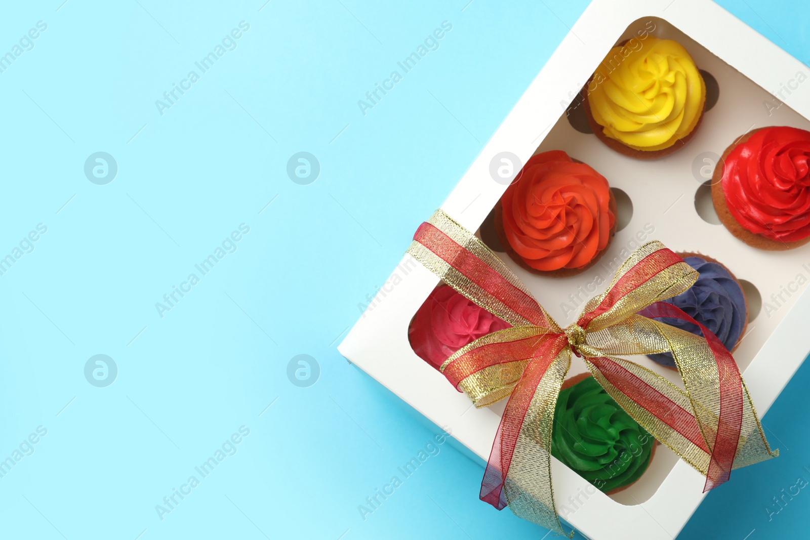 Photo of Box with delicious colorful cupcakes on light blue background, top view. Space for text