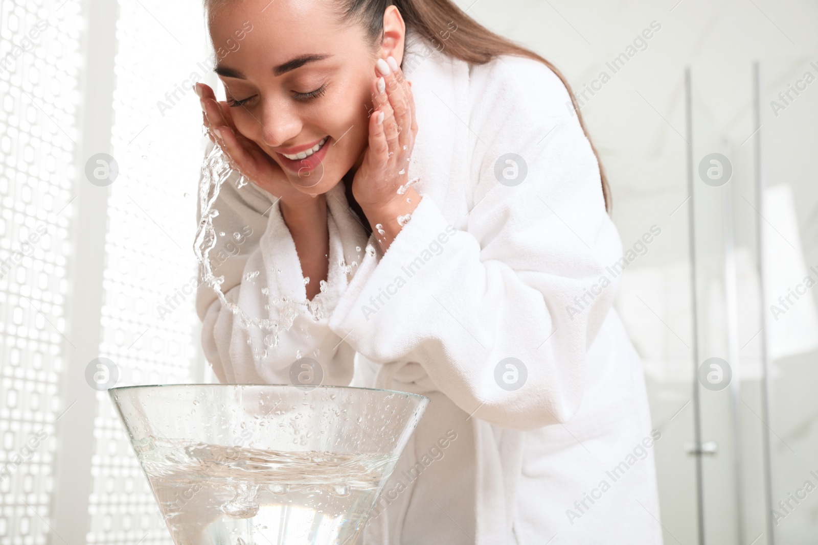 Photo of Beautiful young woman washing her face with water in bathroom