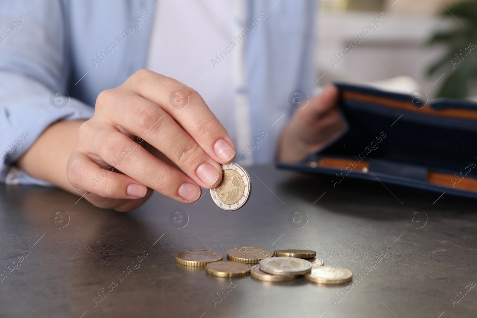 Photo of Poor woman counting coins at grey table indoors, closeup