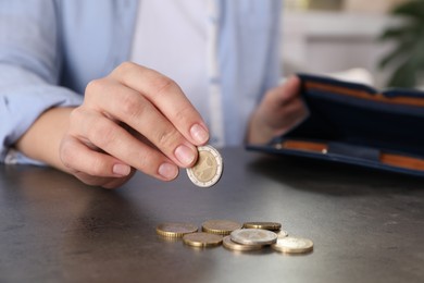 Poor woman counting coins at grey table indoors, closeup