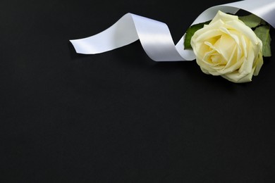 Photo of Beautiful rose and white ribbon on black background, space for text. Funeral symbols