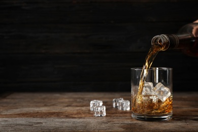 Photo of Pouring whiskey from bottle in to glass with ice cubes on table. Space for text