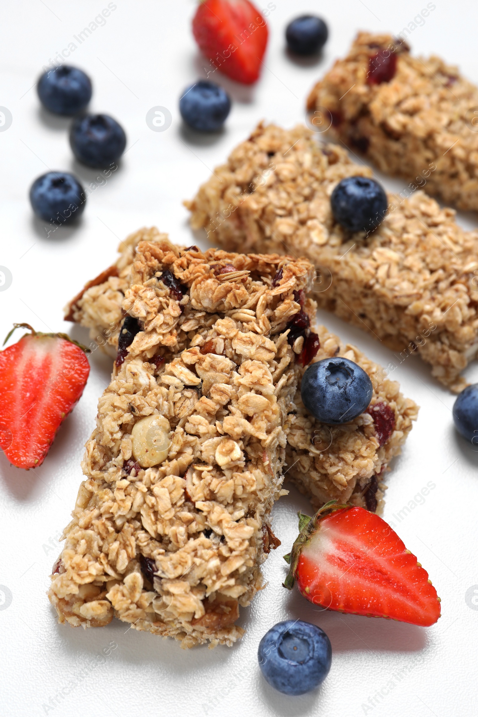 Photo of Tasty granola bars and berries on white table, closeup