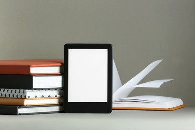 Photo of Modern e-book reader and hard cover books on light grey table