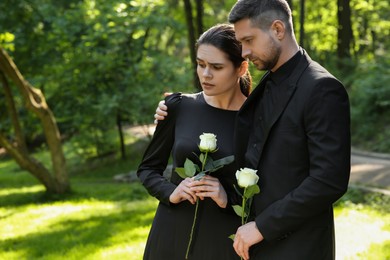 Photo of Sad couple with white rose flowers mourning outdoors, space for text. Funeral ceremony