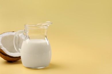 Photo of Glass jug of delicious vegan milk and coconut on yellow background, space for text