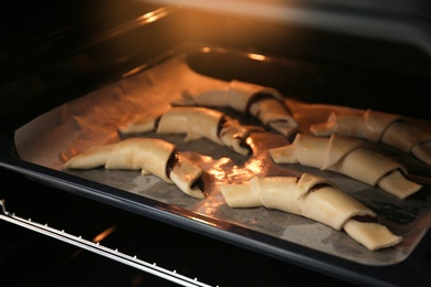 Photo of Baking sheet with raw croissants in oven, closeup