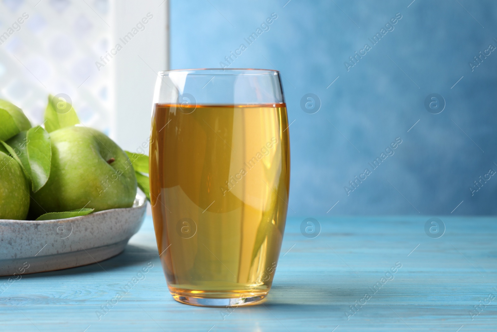 Photo of Glass of fresh juice and apples on light blue wooden table