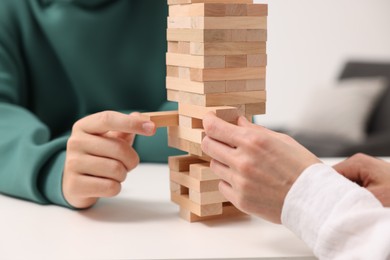 People playing Jenga tower at white table indoors, closeup